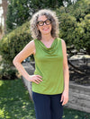 Miik model Liane (5'9", small) smiling wearing Miik's Ada reversible draped cowl neck tank in green moss with a navy pant 