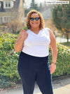 Miik model Carley (5'2", xxlarge) smiling wearing Miik's Ada reversible draped cowl neck tank in white tucked in a navy dressy pant and cool sunglasses 