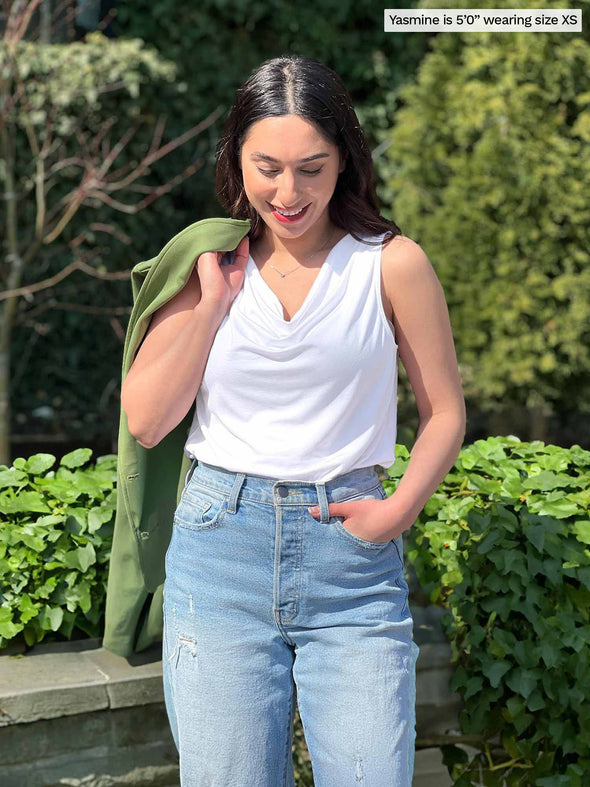 Miik model Yasmine (5'0", xsmall, petite) smiling while looking down wearing Miik's Ada reversible draped cowl neck tank in white with jeans and a green moss blazer over her shoulders 
