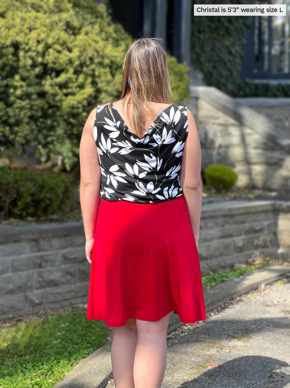 Woman standing with her back towards the camera wearing Miik's Ada reversible draped cowl neck tank in white floral print with a red skirt.