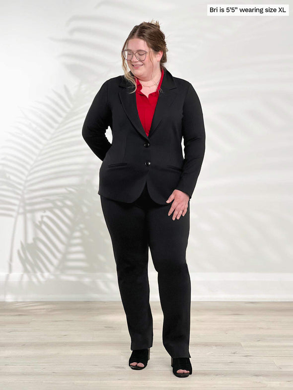 Miik model Bri (5'5", xlarge) smiling and looking away wearing Miik's Adette washable ponte blazer in black with a poppy red collared shirt and black pants