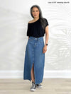 Miik model Lisa (5'6", xsmall) standing in front of a white wall wearing Miik's Adisa reversible slouchy dolman top in black with a long denim skirt 