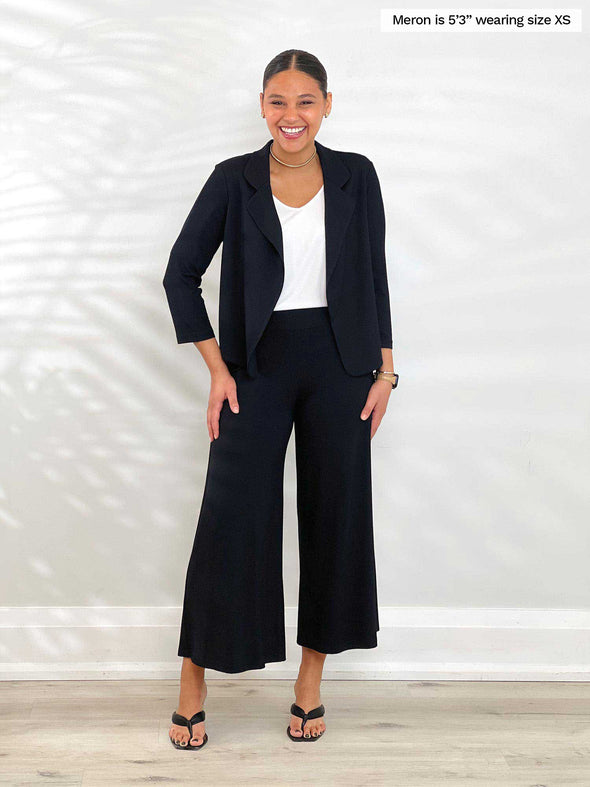 Miik model Meron (5'3", xsmall) smiling wearing Miik's Dorit boxy soft blazer in black with a capri wide leg pant in the same colour and a white tank 