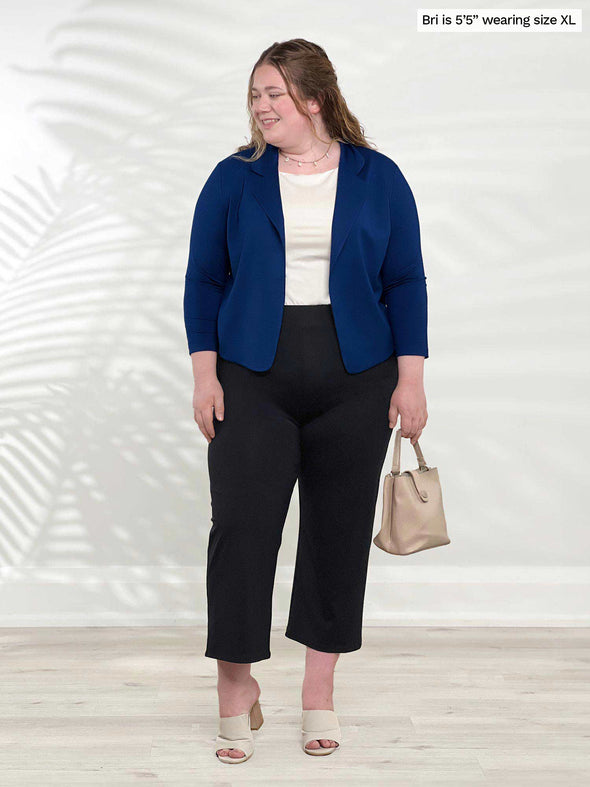 Miik model Bri (5'5", xlarge) smiling and looking away wearing a capri pant in black, a white tank and Miik's Dorit boxy soft blazer in ink blue