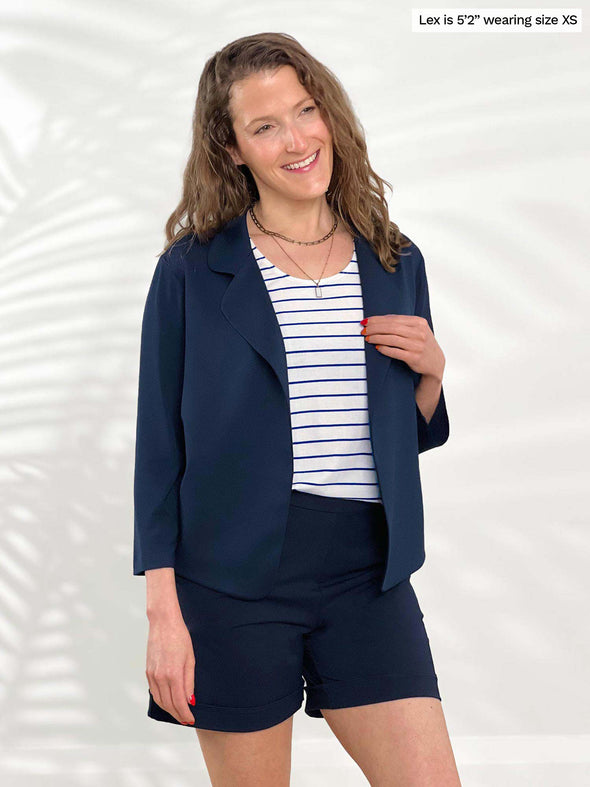 Miik model Lex (5'2", xsmall) smiling wearing Miik's Dorit boxy soft blazer in navy with a short in the same colour and a striped tank 
