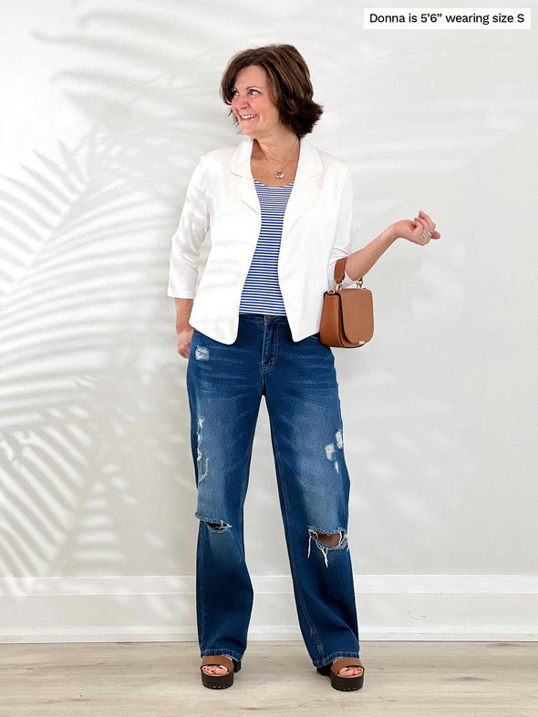 Miik founder Donna (5'6", small) smiling and looking away wearing a ripped wide leg jeans with Miik's Dorit boxy soft blazer in white and a striped cobalt blue tee 