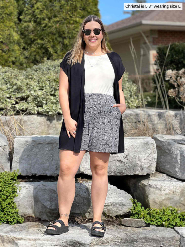 Miik model Christal (5'3", large) smiling wearing Miik's Evie short sleeve pocket cardigan in black with a printed short in pebble and a natural tank top
