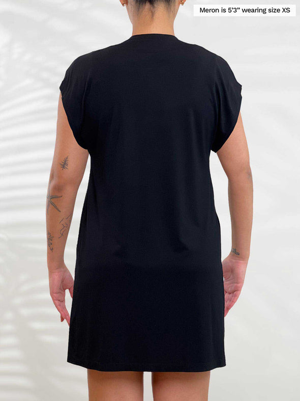 Miik model Meron (5’3”, xsmall) standing with her back towards the camera showing the back of Miik's Evie short sleeve pocket cardigan in black