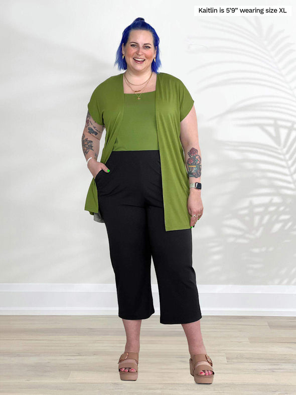 Miik model Kaitlin (5'9", xlarge) smiling wearing Miik's Evie short sleeve pocket cardigan in green moss with a tank top in the same colour and a capri pant in black