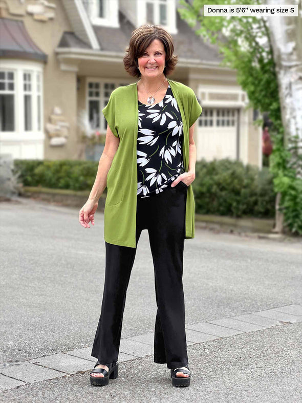 Miik founder Donna (5'6", small) smiling wearing a high waisted pant in black, a white lily tank and Miik's Evie short sleeve pocket cardigan in green moss 