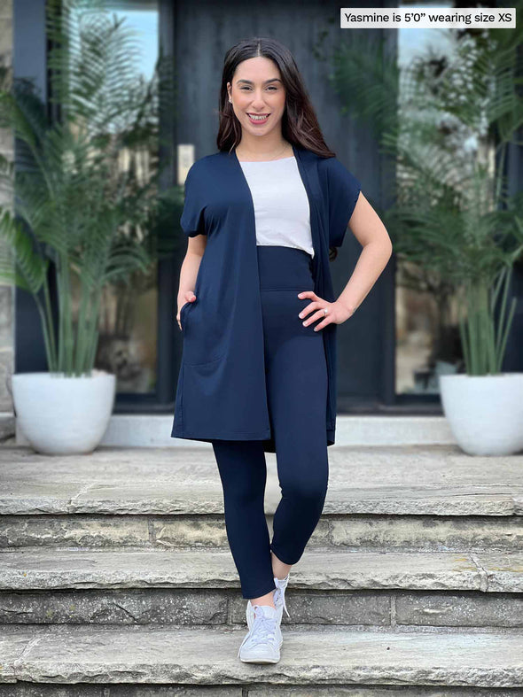 Miik model Yasmine (5'0", xsmall, petite) smiling wearing Miik's Evie short sleeve pocket cardigan in navy with a legging in the same colour and a white tee 