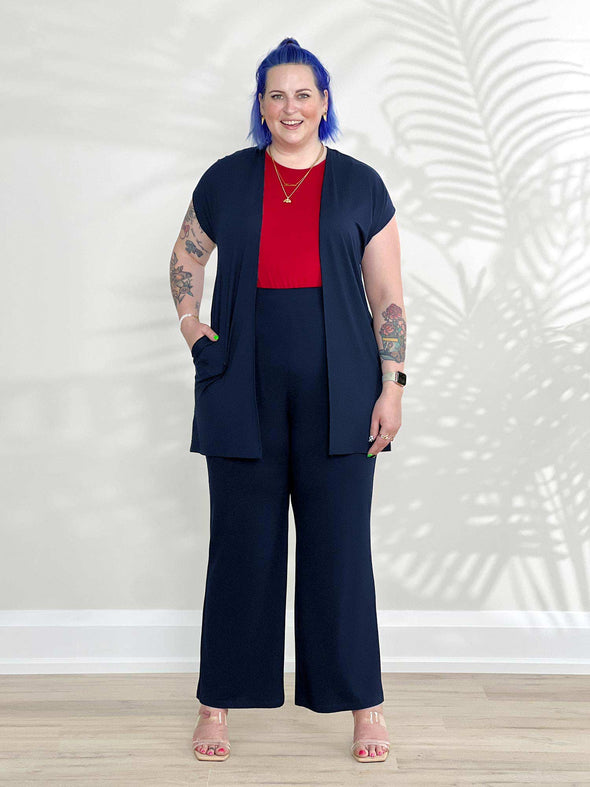 Miik model Kaitlin (5'9", xlarge) smiling wearing Miik's Evie short sleeve pocket cardigan in navy with a pant in the same colour and a poppy red tank 