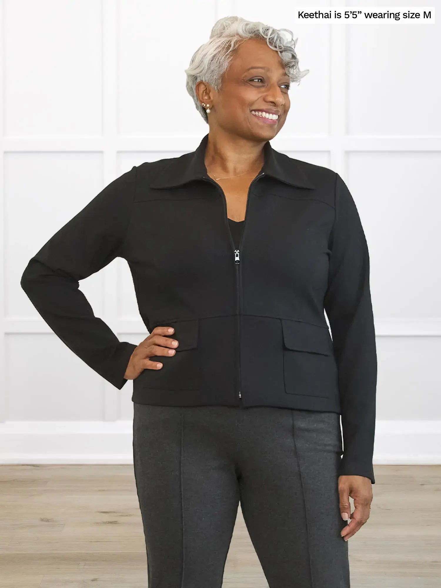 Woman wearing a black jacket and gray pants against a white background