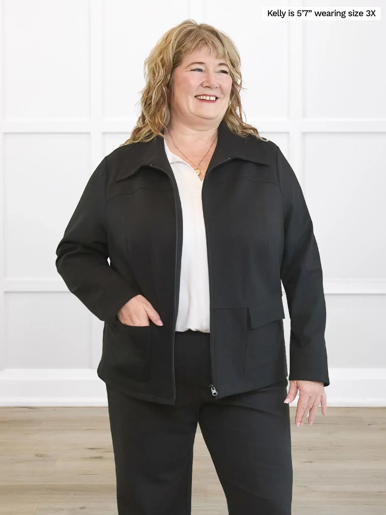 Woman wearing a black coat and pants against a white wall.