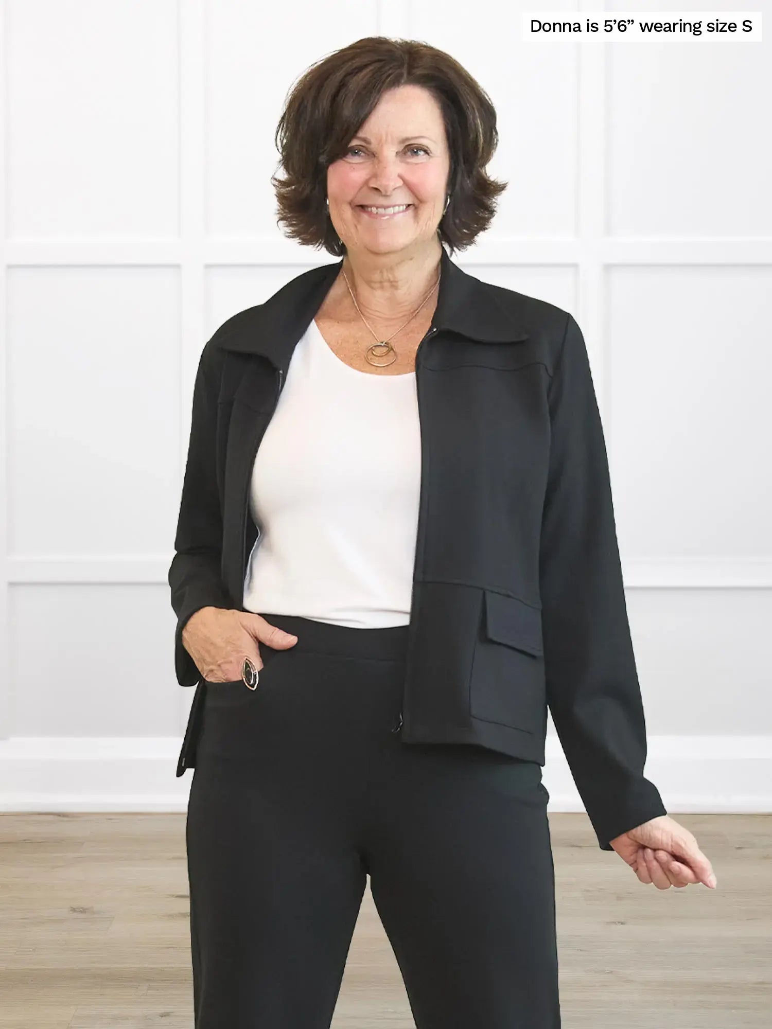 Woman wearing a black jacket and black pants against a white background