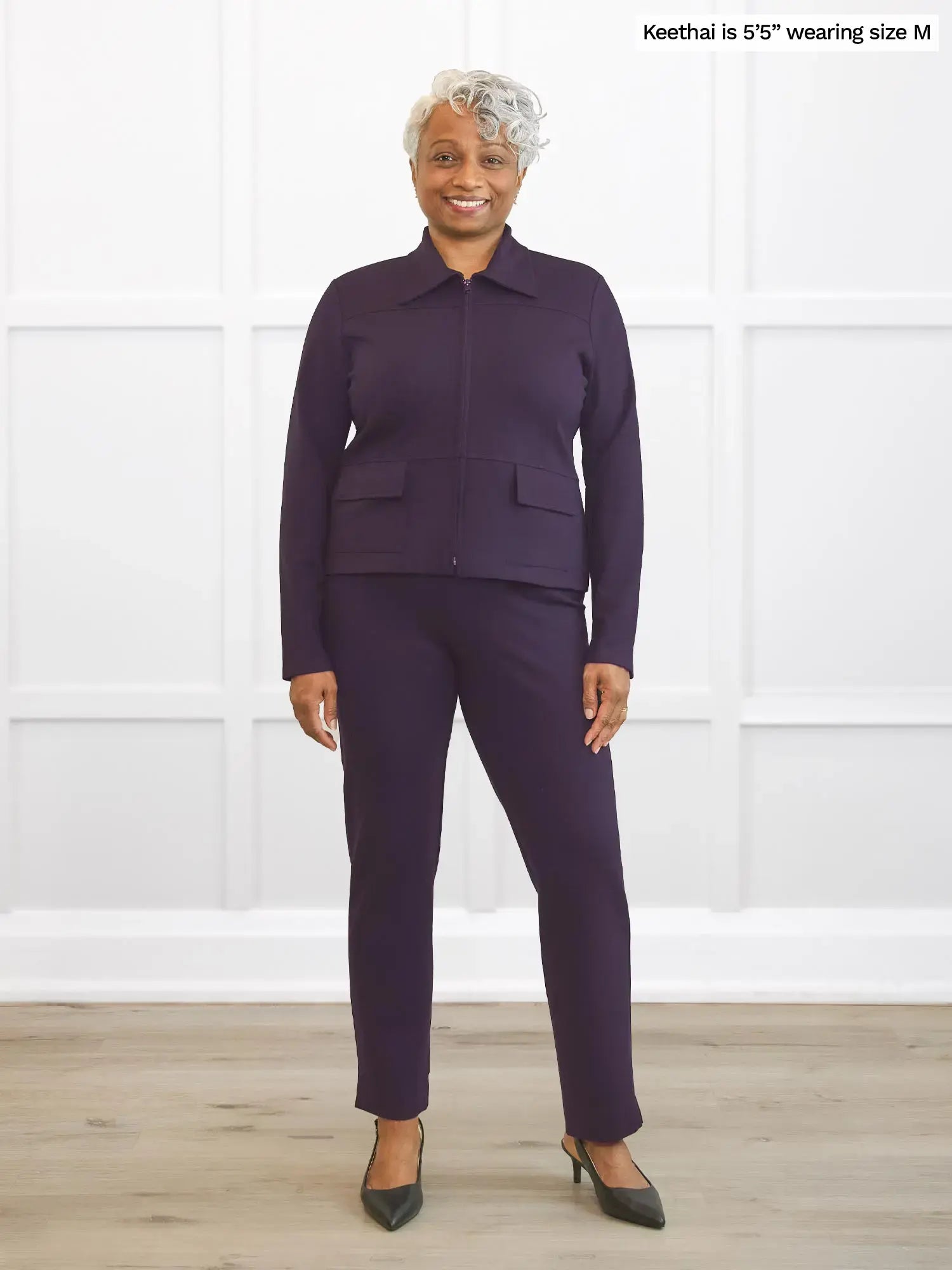 Woman wearing a purple suit standing against a white wall.