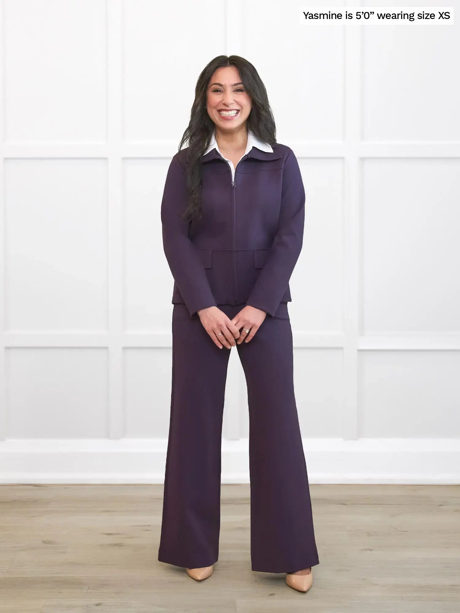 Woman wearing a purple outfit with a white shirt against a white wall.
