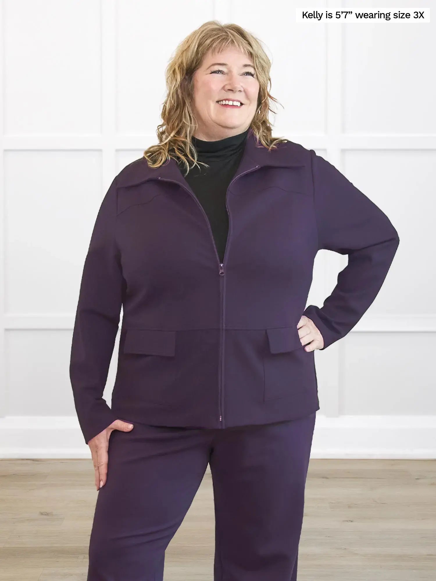 Woman wearing a purple outfit standing against a white wall.