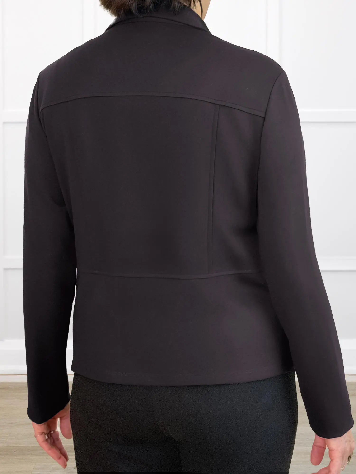 Back of a dark brown jacket worn by a person on a white background