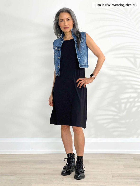 Miik model Lisa (5'6", xsmall) smiling wearing Miik's Jaaron reversible tank dress in black and boots in the same colour and a denim vest 