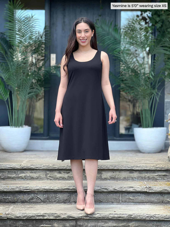 Miik model Yasmine (5'0", xsmall, petite) smiling wearing Miik's Jaaron reversible tank dress in black