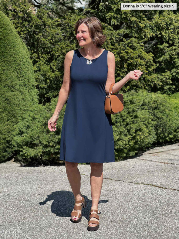Miik founder Donna (56", small) smiling and looking away wearing Miik's Jaaron reversible tank dress in navy with a brown purse