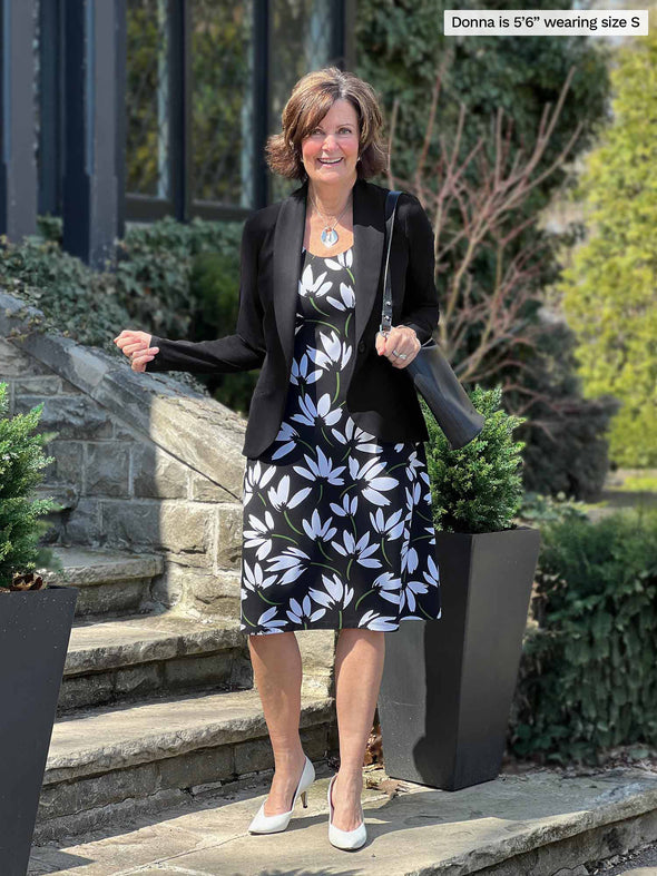 Miik founder Donna (56, small) standing on a stairway smiling wearing Miik's Jaaron reversible tank dress in white lily print with a black blazer 