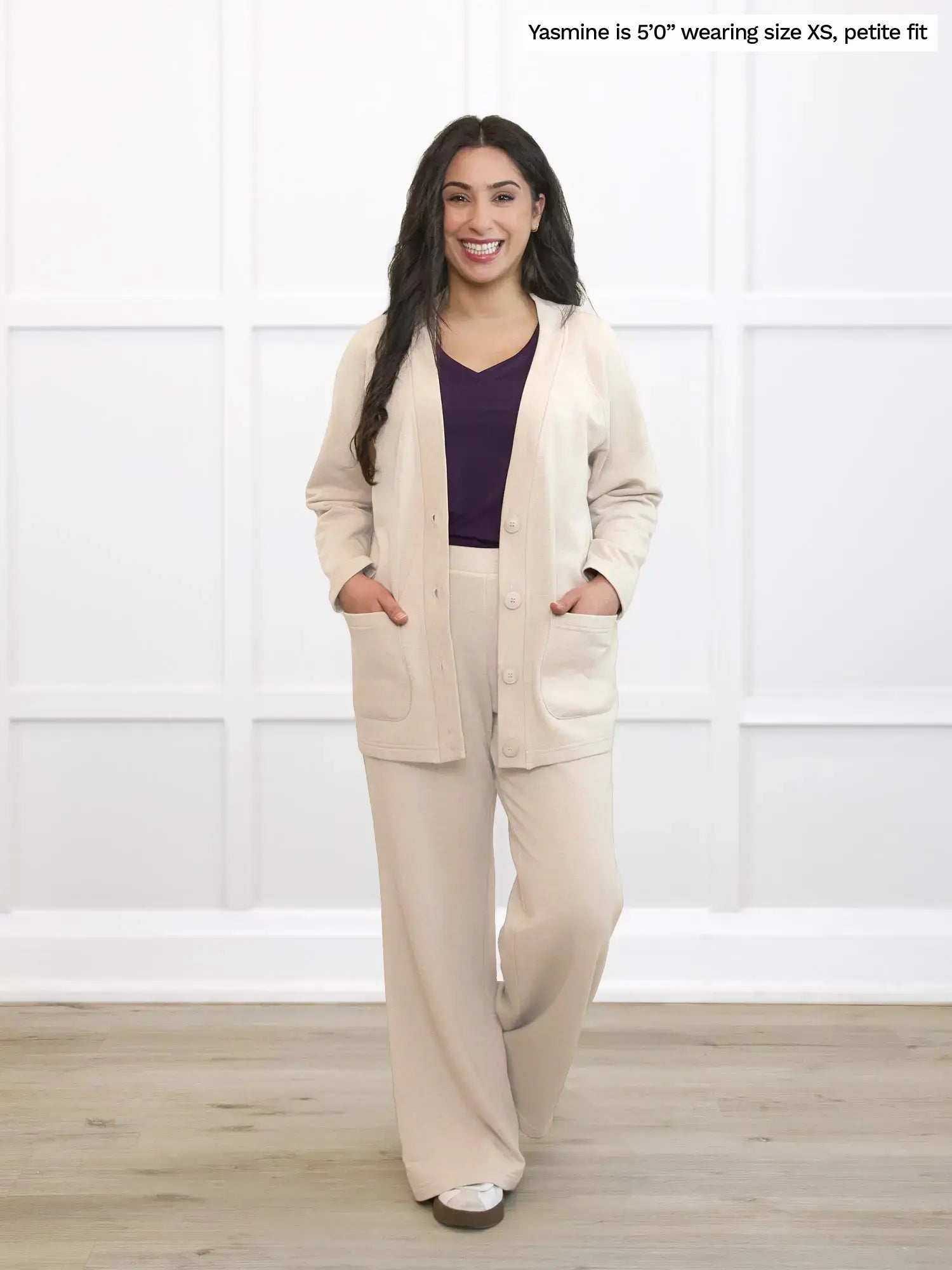 Woman wearing a beige lounge suit with a purple top in a white room.