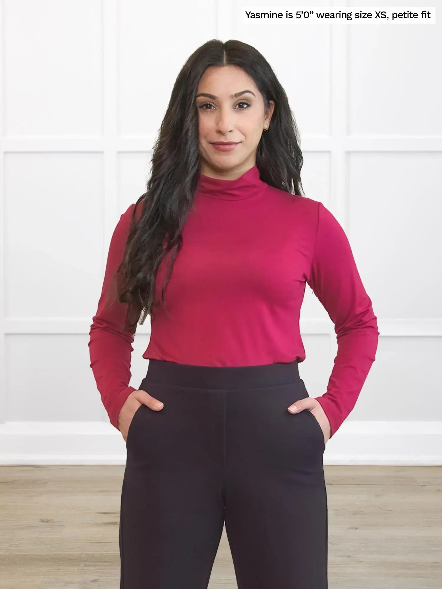 Woman wearing a red long-sleeve top and dark brown petite pants against a white background