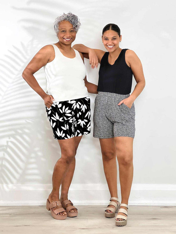 Miik models Keethai and Meron smiling while standing next to each other both wearing the same Miik's Kavya pull-on casual print shorts but in different prints. Keethai is wearing in while lilt white Meron is wearing in pebble. They are also both wearing tank tops 