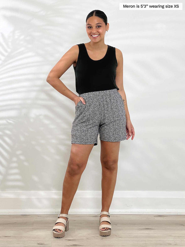 Miik model Meron (5'3", xsmall) smiling wearing a black tank top tucked in Miik's Kavya pull-on casual print shorts in pebble print 