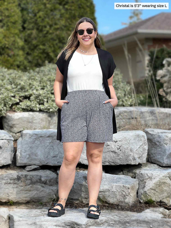 Miik model Christal (5'3", large) smiling wearing Miik's Kavya pull-on casual shorts in pebble print with a natural tank top and short sleeve cardigan in black