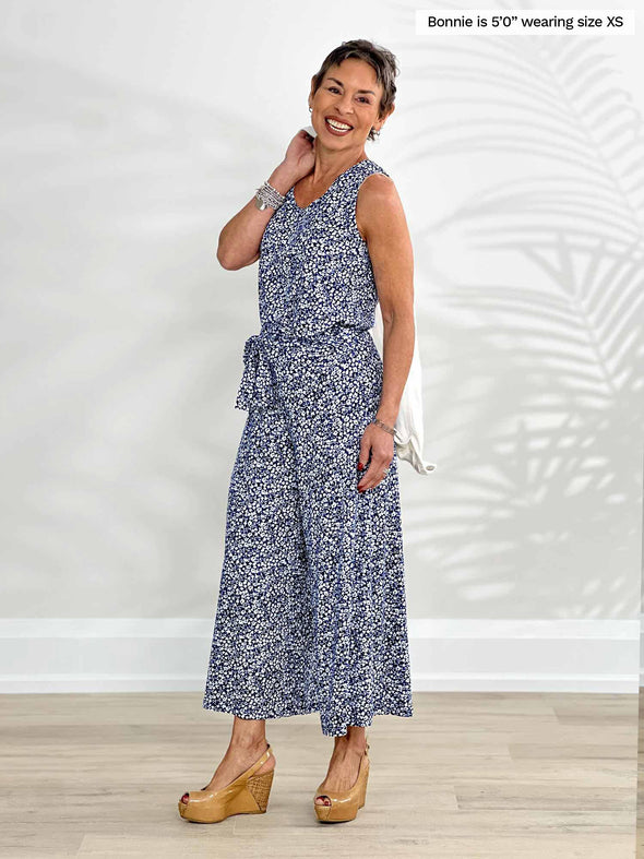 Miik model Bonnie (5'0", xsmall, petite) smiling while standing in front of a white wall wearing Miik's Kimmay open-back capri jumpsuit in baby's breath print