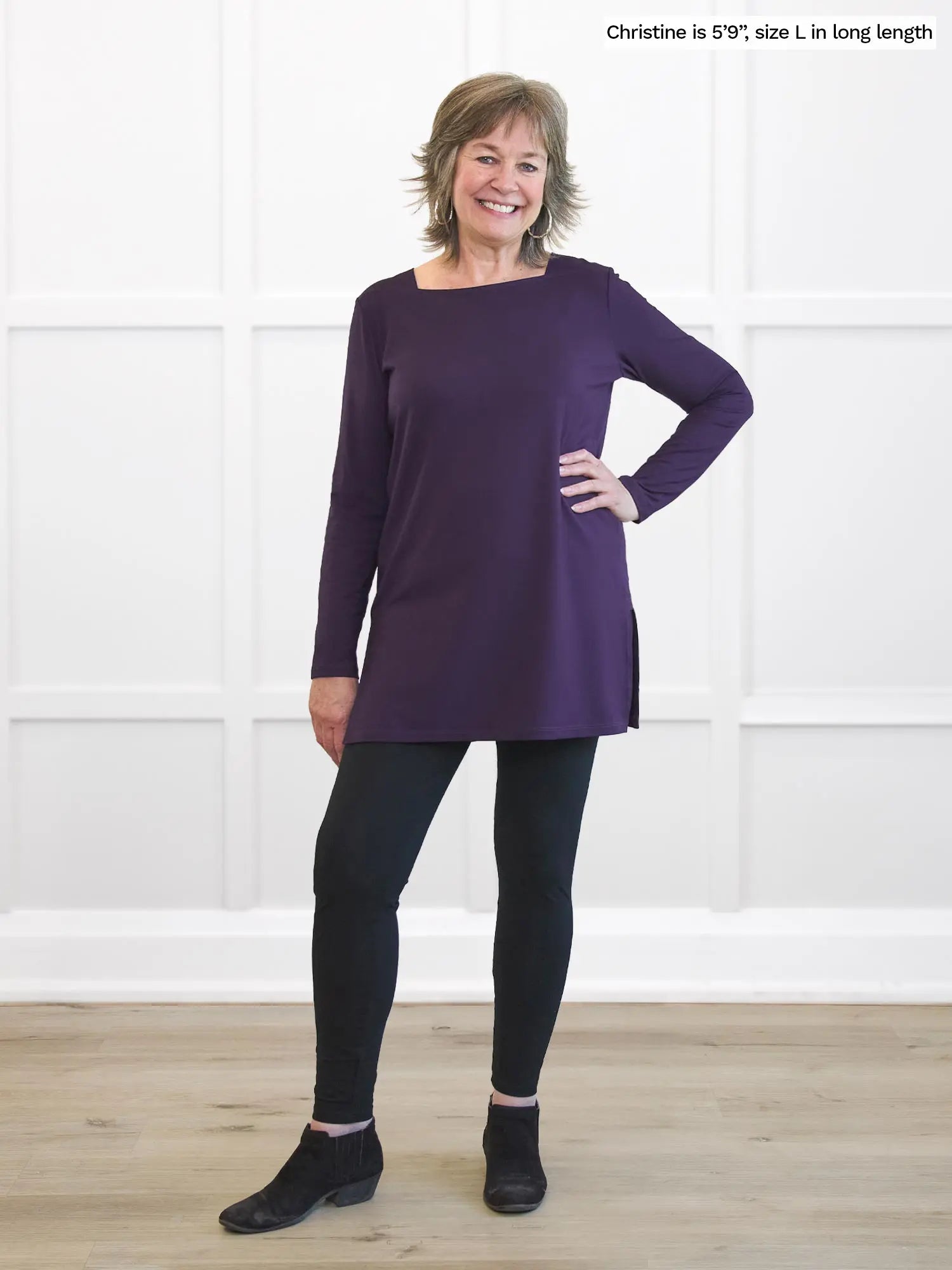 Woman wearing a purple long-sleeve dress against a white wall.