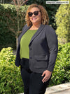 Miik model Carley (5'2", xxlarge) smiling while standing sideway wearing Miik's Maeve LightLuxe washable blazer in graphite with a green moss tank and a black jeans