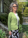 Woman standing in nature wearing Miik's Maeva LightLuxe washable blazer in moss green over a white blouse and floral pants.