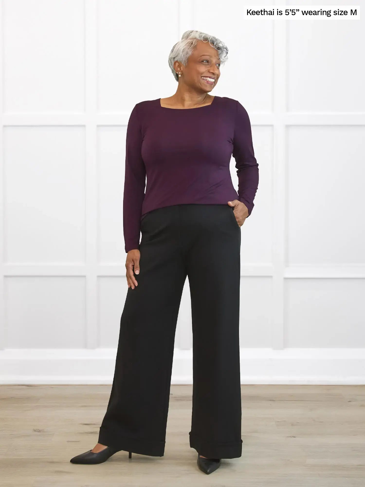 Woman wearing a purple long-sleeve top and black pants against a white background