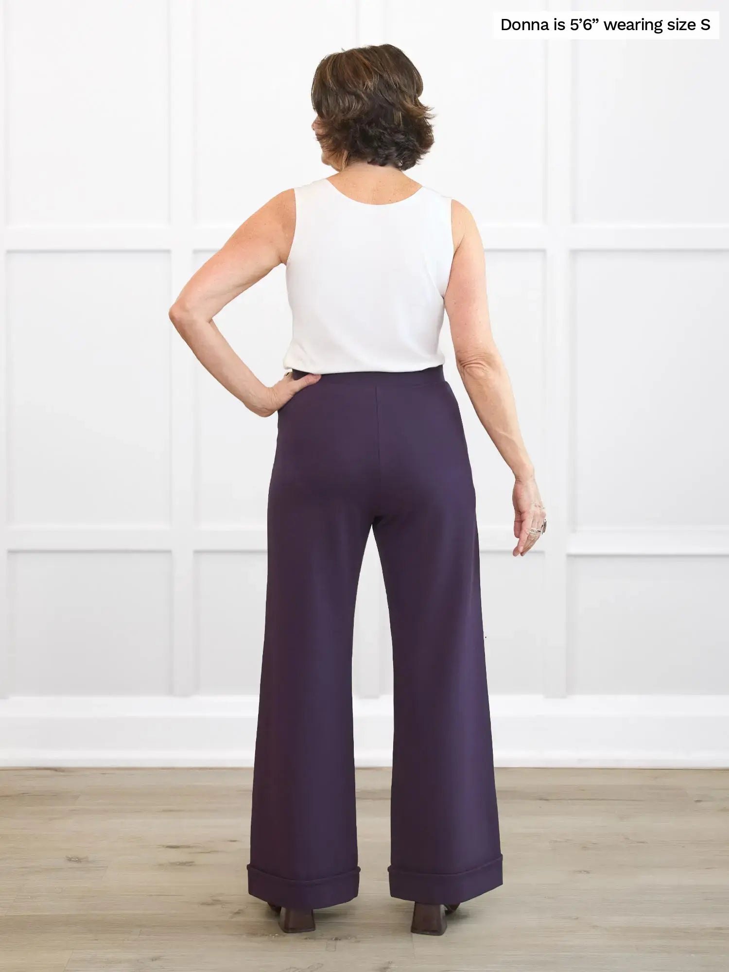 Woman wearing a white top and purple pants against a white background