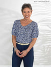 Miik model Bonnie (5'0", xsmall, petite) smiling wearing Miik's Makena v-neck puff sleeve blouse in baby's breath print with a navy pant 