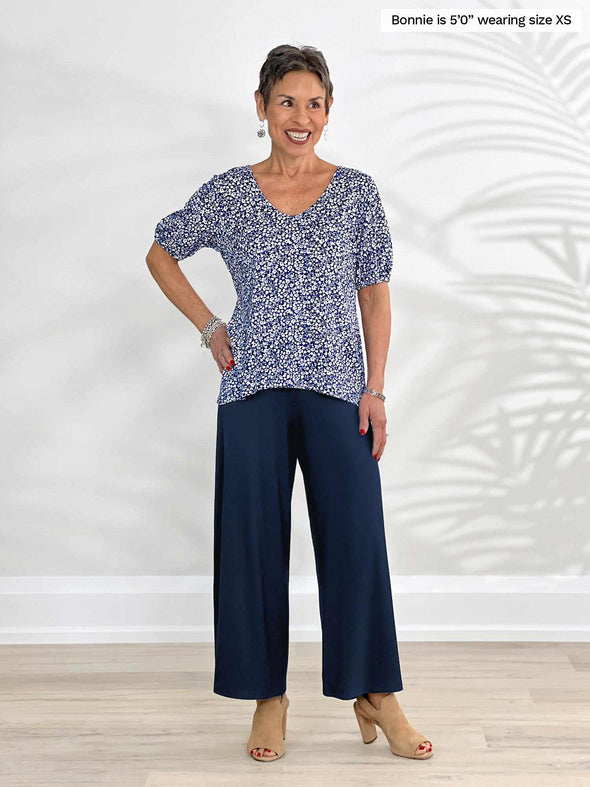 Miik model Bonnie (5'0", xsmall, petite) smiling wearing a wide leg capri pant in navy with Miik's Makena v-neck puff sleeve blouse in baby's breath print