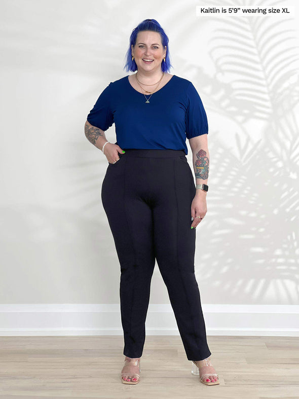 Miik model Kaitlin (5'9", xlarge) smiling wearing Miik's Makena v-neck puff sleeve blouse in ink blue tucked in a black dress pant