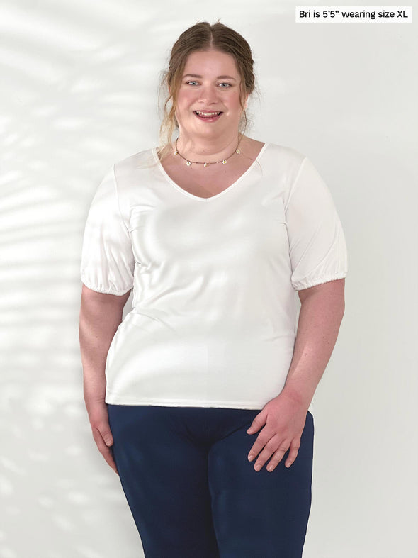 Miik model Bri (5'5", xlarge) smiling wearing Miik's Makena v-neck puff sleeve blouse in white with a navy pant 