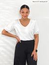 Miik model Meron (5'3", xsmall) smiling wearing Miik's Makena v-neck puff sleeve blouse in white tucked in a black pant 