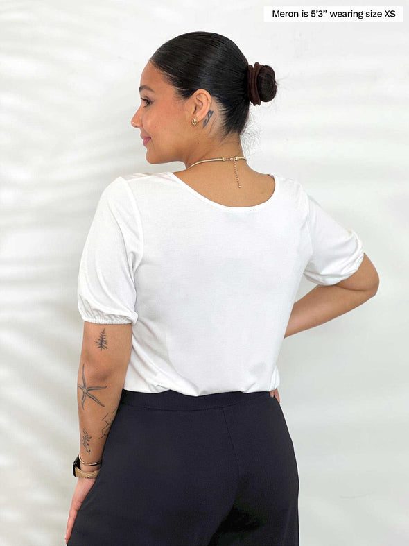 Miik model Meron (5’3”, xsmall) standing with her back towards the camera showing the back of Miik's Makena v-neck puff sleeve blouse in white 