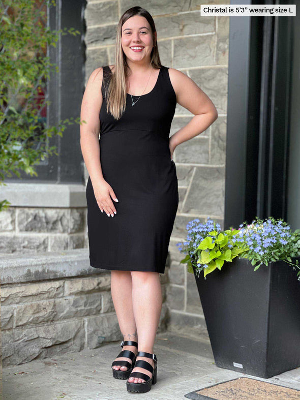 Miik model Christal (five feet three, large) standing in front of a brick wall smiling wearing Miik's Maryse reversible sweetheart dress black reversed with matching colour sandals 