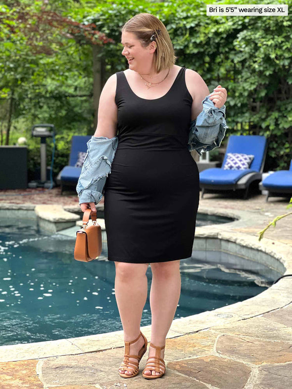 Miik model Bri (five feet five, xlarge) standing in front of a pool while looking away wearing Miik's Maryse reversible sweetheart dress black reversed along with a denim jacket