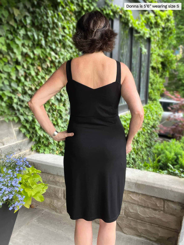 Miik founder Donna (five feet six, small) tanding with her back towards the camera showing the back of Miik's Maryse reversible sweetheart dress in black, when the scoop neckline is worn in the front and the sweetheart in the back