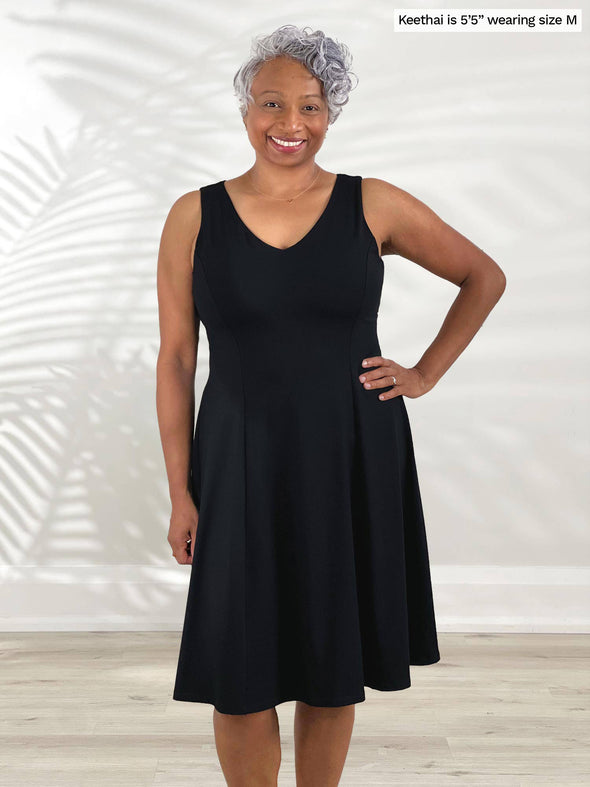 Miik model Keethai (5'5", medium) smiling wearing Miik's Niah reversible knee length flounce dress in black 