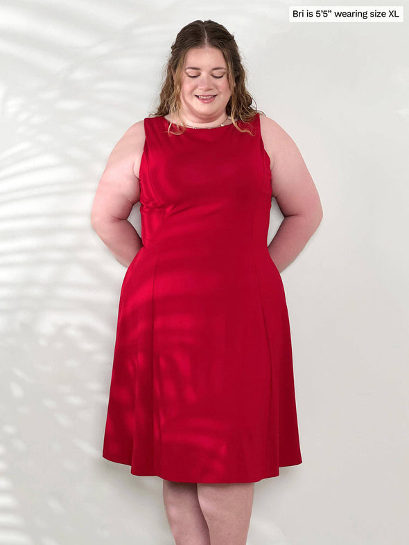 Miik model Bri (5'5", xlarge) smiling and looking down wearing Miik's Niah reversible knee length flounce dress in poppy red