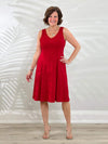 Miik founder Donna (5'6", small) smiling while standing in front of a white wall wearing Miik's Niah reversible knee length flounce dress in poppy red